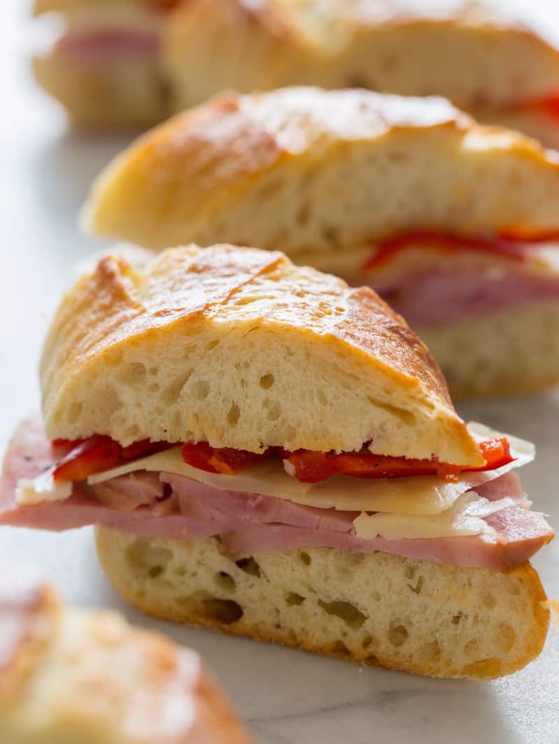 A close up of bocadillo bites of ham, cheese, and pickled cherry peppers on a baguette.