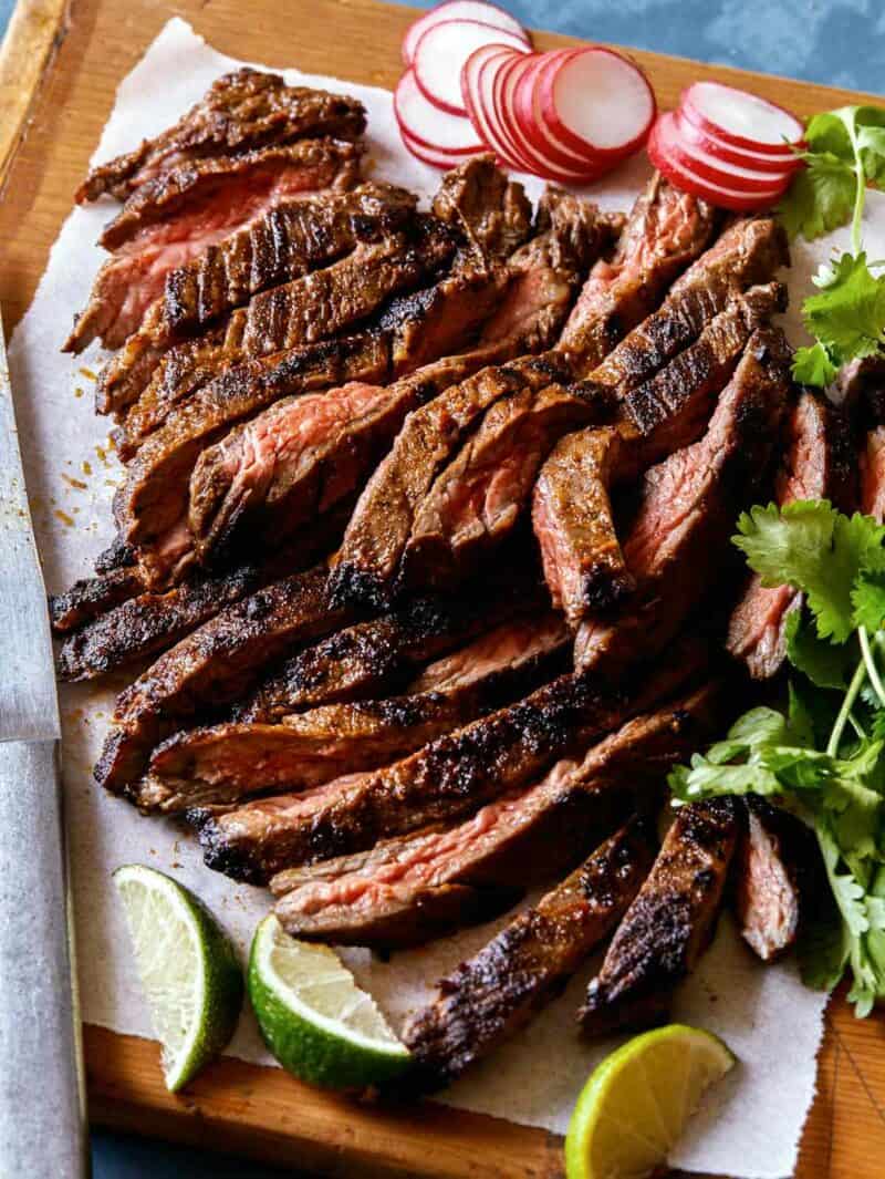 Carne Asada recipe cut up on a cutting board with lime wedges and a knife.