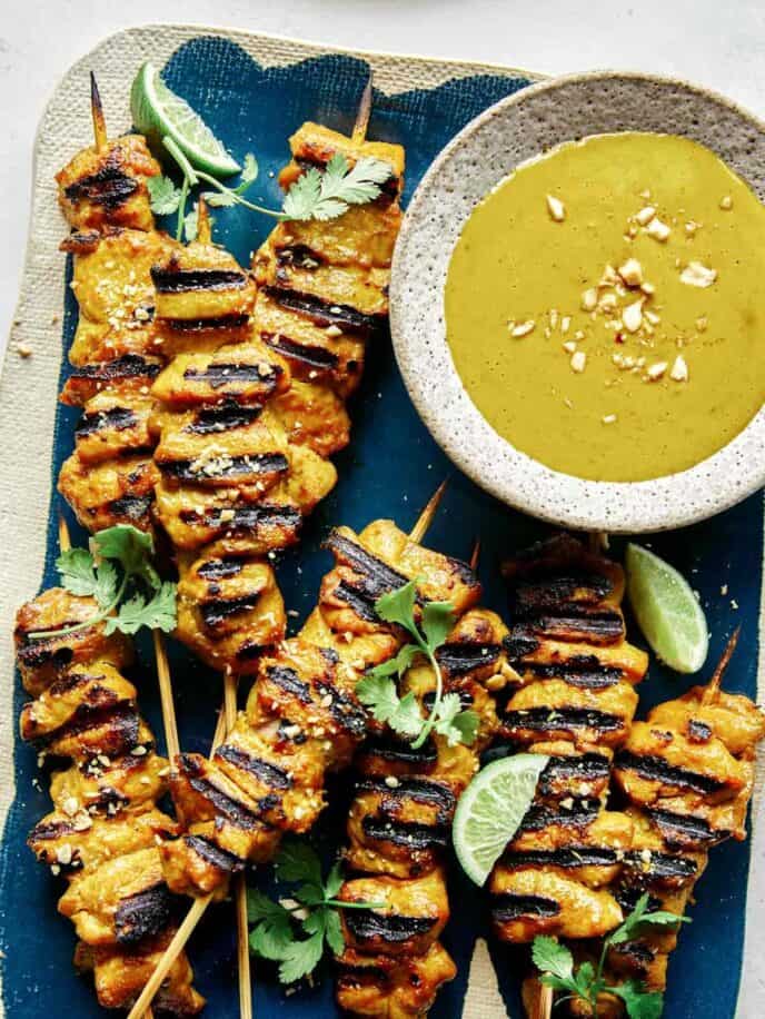 Chicken satay on a platter with lime wedges.
