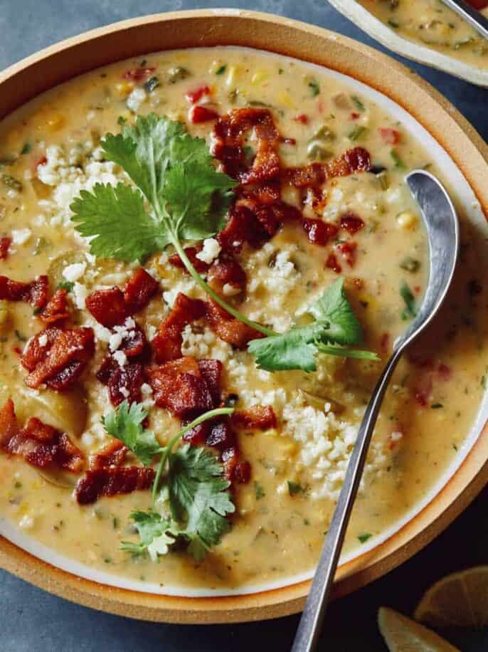 A bowl of corn chowder garnished with bacon and cilantro with a spoon.